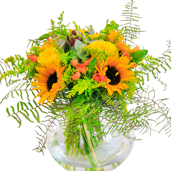 The impression this bouquet leaves is one of golden exuberance, capturing the best of an Emerson Park summer afternoon. Sunflowers and yellow garden roses share centre stage, each bloom opening wide to reveal plush, sun-drenched petals. Interwoven with lush greens, you'll spot graceful tendrils and feathery ferns that fall like soft shadows, creating a sense of movement and gentle wildness-evoking the small, hidden gardens found near Brentwood Road. Among the vivid blossoms, glossy red Hypericum berries add pops of colour, their smooth surfaces reflecting the light and heightening the arrangement's joyful mood. Subtle blue-green eucalyptus leaves peek out, enhancing the bouquet's rustic charm and filling the air with a whisper of freshness. Every stem stands firmly in a clear, round glass vase, allowing the organic puzzle of green stems to intertwine below the water's surface. Up close, the tactile differences delight: the soft suede of sunflower petals, the crisp snap of fresh foliage, the rounded coolness of the berries. This bouquet is the kind florists love to craft for significant occasions-anniversaries, congratulations, or any event deserving the gift of sunshine and delight, all delivered with the care and personal touch of Emerson Park Florist.